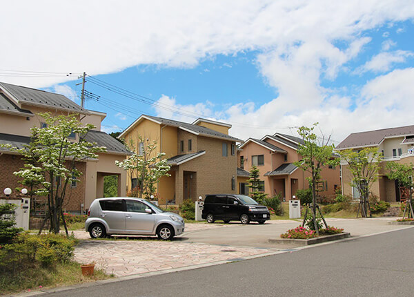 青空の下に建ち並ぶ住宅街の家々と乗用車