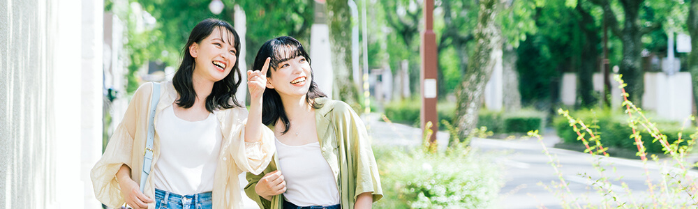 モデルコースの紹介ページへ 緑豊かな並木道を、笑顔で指をさしながら歩く女性二人組