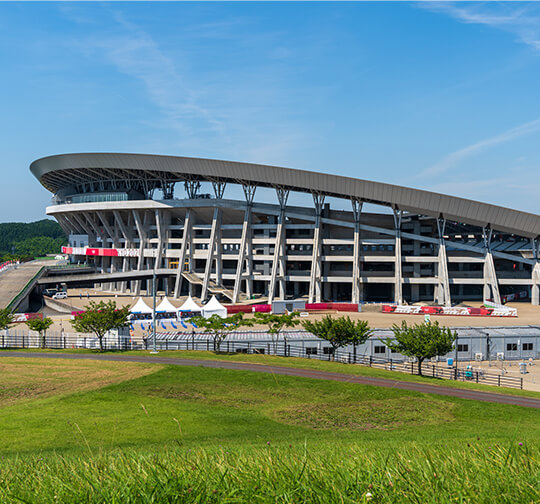 青空の下緑の芝生越しに望む巨大なキューアンドエースタジアム