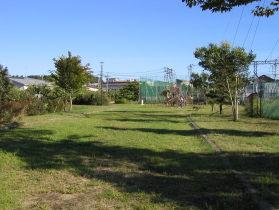 奥には緑のネットで作られたフェンスが見えていて、手前には芝生の広場がある写真