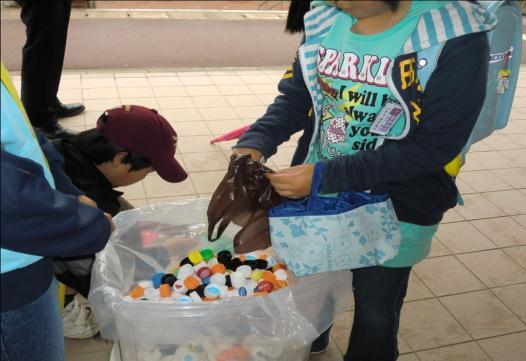 ペットボトルのキャップが集められた大きな袋に、持参したペットボトルのキャップを入れている子供の写真