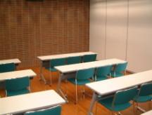 白い机と緑の椅子が並ぶ研修室の写真