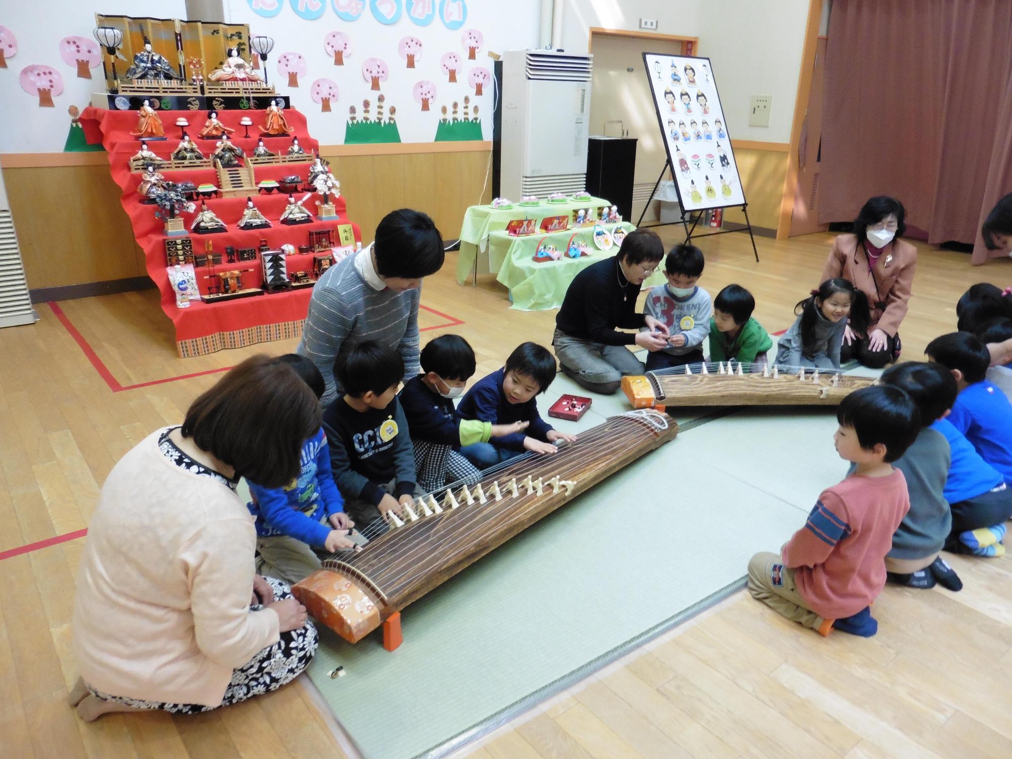 七段飾りのお雛様と琴の演奏を教わっている園児たちの写真